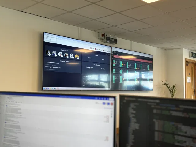 Wall-mounted service desk and infrastructure monitoring dashboards above office workstations.